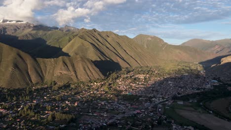 drone shot of sacred valley with village and gigantic mountain range lighting by sun in cusco, peru