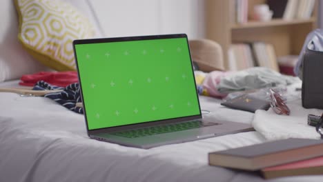 portátil de pantalla verde con maleta abierta en la cama en casa siendo empacado para las vacaciones de verano 2