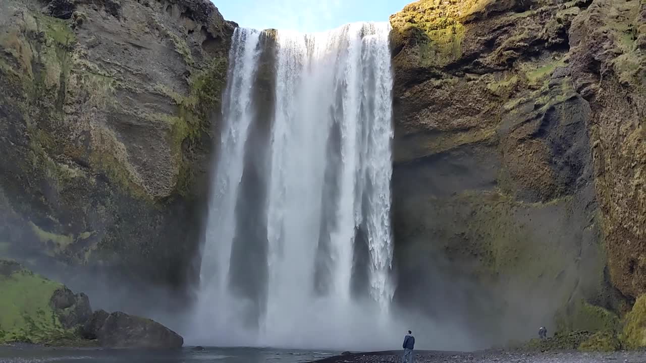 cascada de skogafoss en islandia en verano con un hombre caminando a lo largo del río