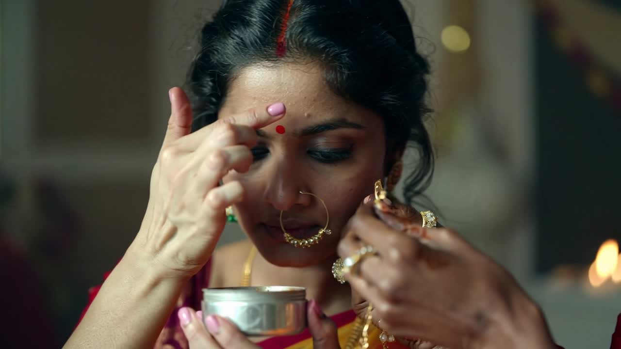 Picking sindoor container during wedding prep, bride applying vermilion, mother fastening choker