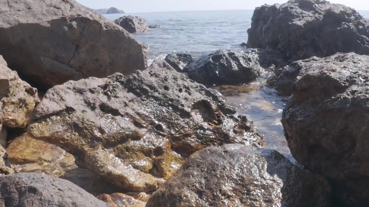 Piccole onde che si infrangono dolcemente su rocce vulcaniche su una spiaggia soleggiata.