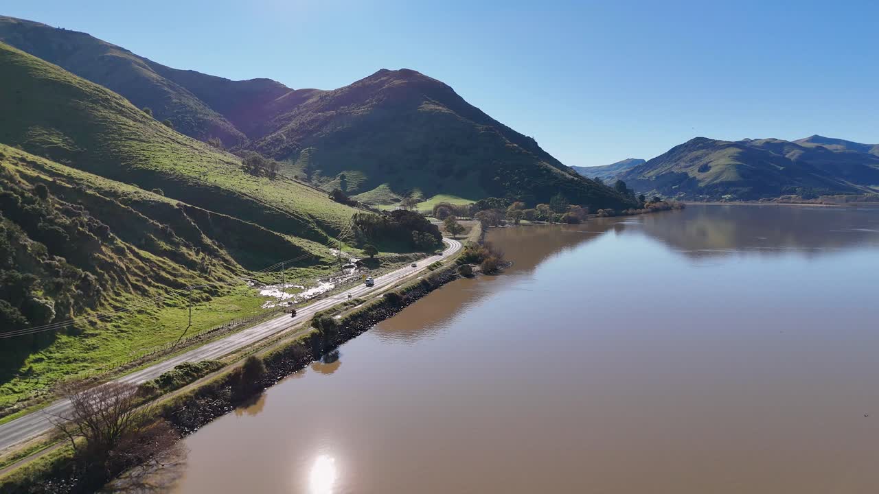 Aerial footage captures serene Lake Forsyth with surrounding hills under clear blue skies in Akaroa, New Zealand