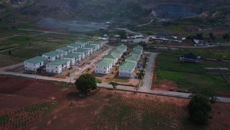 drone video captures an aerial view of modern residential complexes amidst lush fields in abuja, nigeria, under soft daylight, highlighting architecture and serene landscape. quarry can be seen behind