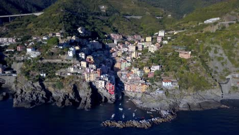 Riomaggiore-Cinque-Terre-Italian-coastline-with-residential-buildings-on-the-cliffside,-Aerial-dolly-out-reveal-shot