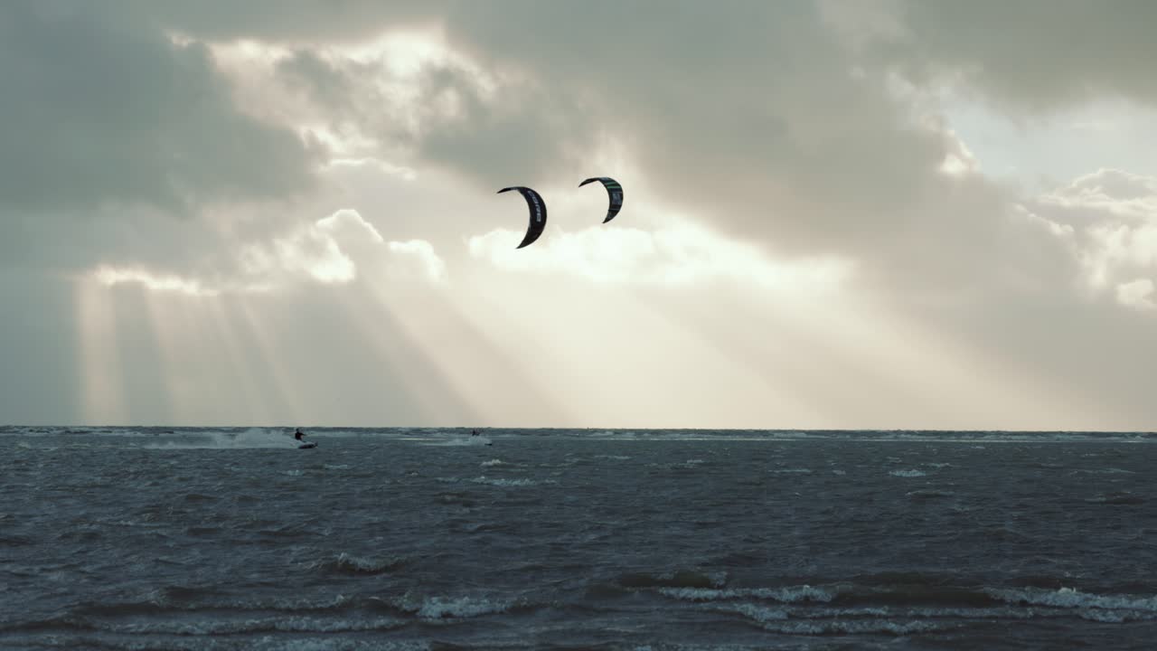 kitesurfers triturando en tormenta, mientras el sol brilla a través de nubes oscuras