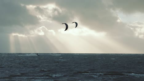 Kitesurfers-shredding-in-storm,-while-sun-beams-through-dark-clouds