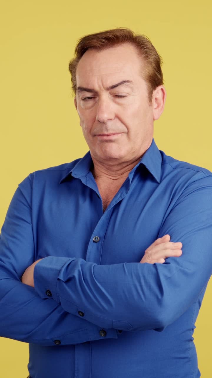 Portrait of a Middle-Aged Man in Blue Shirt with Crossed Arms Against a Yellow Background