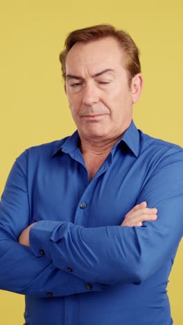portrait of a middle-aged man in blue shirt with crossed arms against a yellow background
