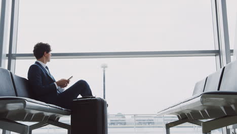 homem de negócios sentado na sala de embarque do aeroporto usando um telefone celular