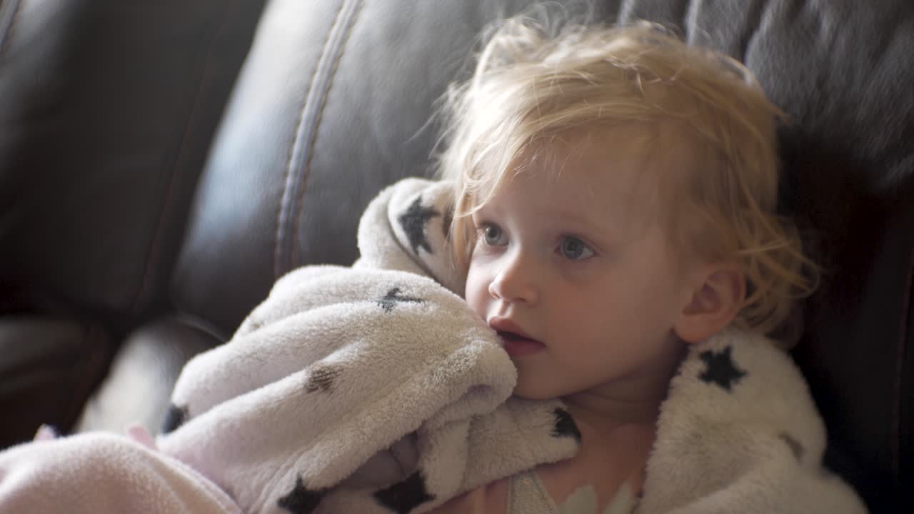 Bambina con i capelli spettinati che guarda la televisione tenendo la sua copertina di sicurezza - ritratto ravvicinato statico