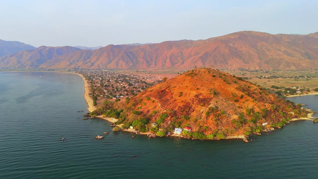 Une vue aérienne autour de la colline distinctive d'Usisya révèle le village, le lac Malawi bleu-vert, la terre rougeâtre et des montagnes dénudées et accidentées