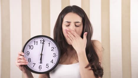 a close-up of a sleepy girl. the girl is holding a wall clock and moves the clock hand.