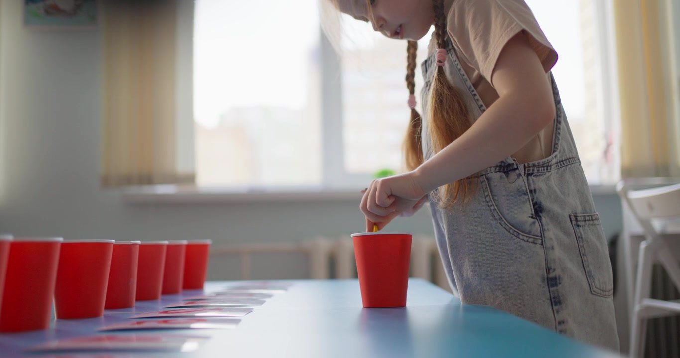 Young Girl Playing Educational Game with Red Cups and Sticks