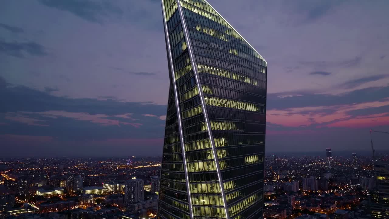 Aerial video shot of a modern skyscraper at dusk, showcasing its unique twisted design