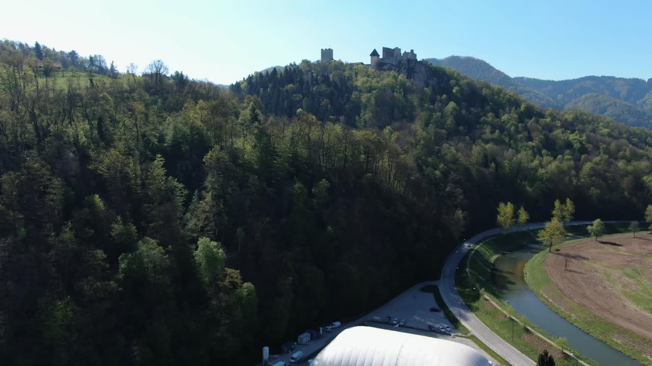 Flight over small village to a castle on top of a mountain surrounded by a thick forest. Drone shot
