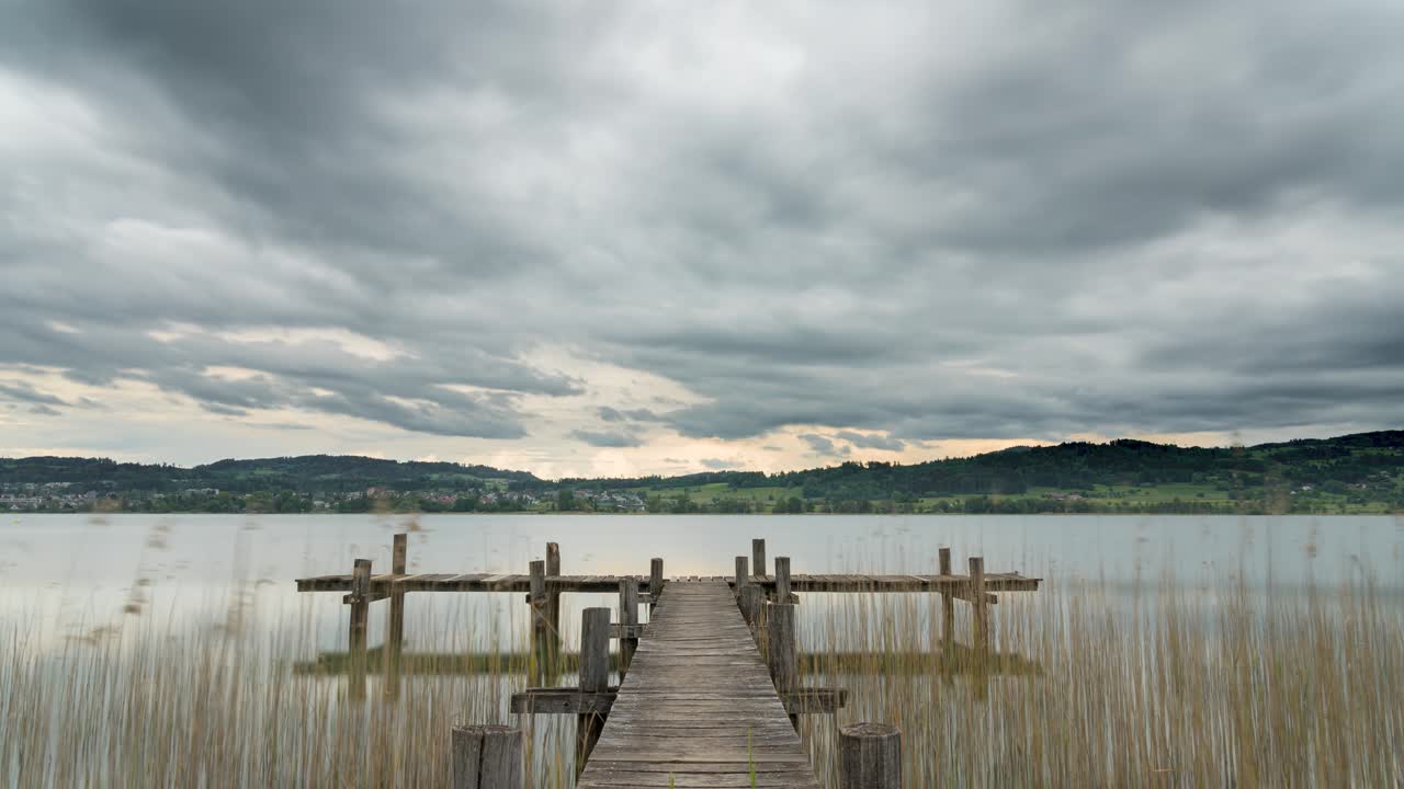 el muelle de madera en forma de t se extiende hasta el lago rural de pfäffikersee, suiza, mientras las nubes grises se precipitan por el cielo.
