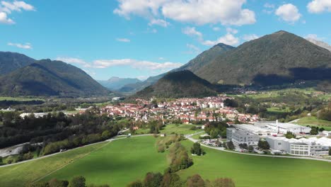 Aerial-view-of-Tolmin-town-with-industry-buildings-in-foreground,-castle-ruin-and-mountains-in-background-on-sunny-summer-day