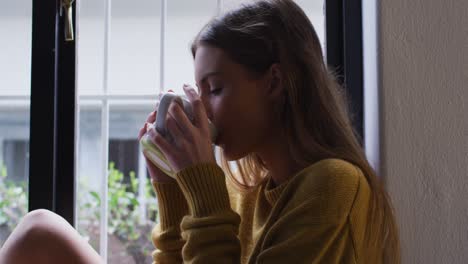 Frau-Trinkt-Kaffee,-Während-Sie-Zu-Hause-Aus-Dem-Fenster-Schaut