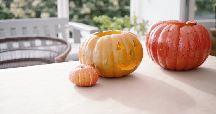 La cámara hace un paneo hacia la derecha en el porche para revelar una calabaza roja y una calabaza de Halloween iluminada sobre una mesa