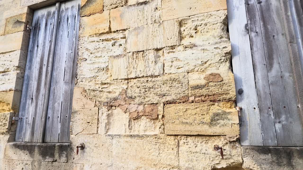 La telecamera a mano panoramica su muri in pietra consumati e persiane in legno in un villaggio storico francese.
