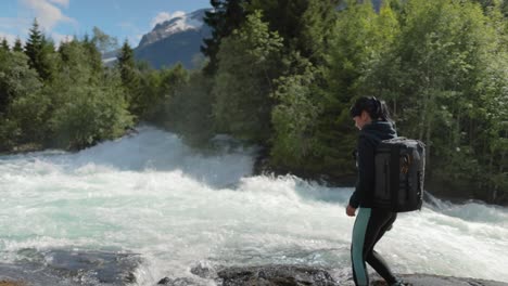 viajera con una mochila, bebiendo agua en la naturaleza en el bosque cerca de un río de montaña.
