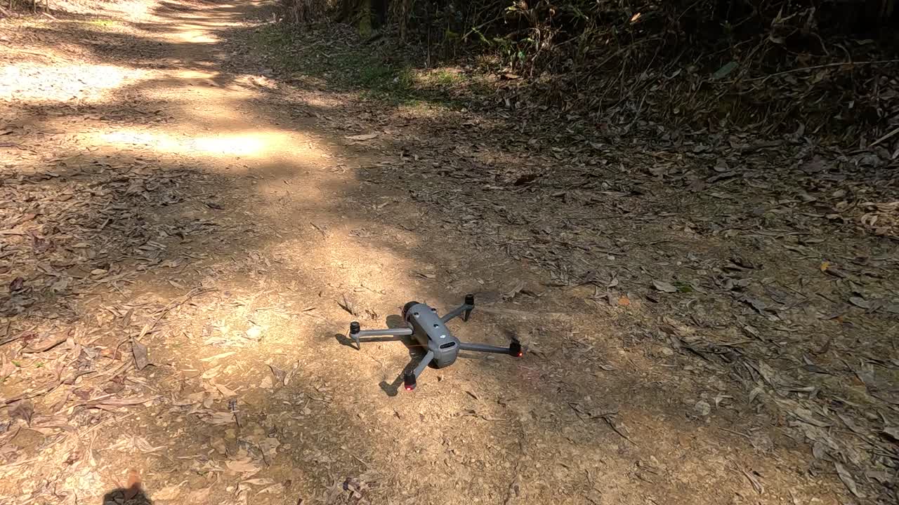 A drone gently lands on a sunlit dirt path in the Daintree Rainforest, surrounded by lush greenery and dappled sunlight