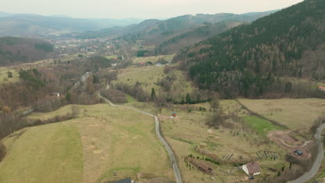 An-aerial-shot-captures-the-serene-landscape-of-Jedlina-Zdrój,-nestled-in-a-valley-with-residential-areas-amid-forested-hills