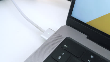 beautiful close-up and slow motion shot of a young man's hand connecting the charger of a macbook pro 2024 computer on a white table