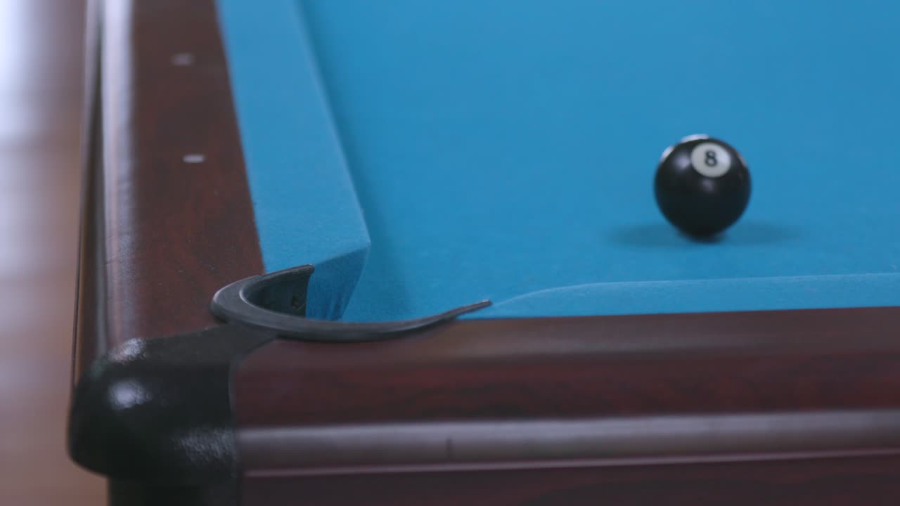hombre hundiendo última bola de 8 tiros en el bolsillo de la esquina en la mesa de billar azul