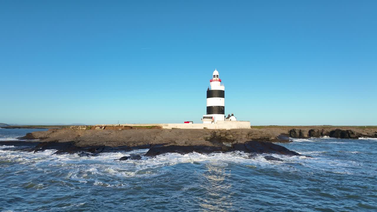 Faro di Hook Head, Wexford, Irlanda, ripresa aerea con panoramica a destra, dal mare e sotto cieli blu, in un giorno di primavera.