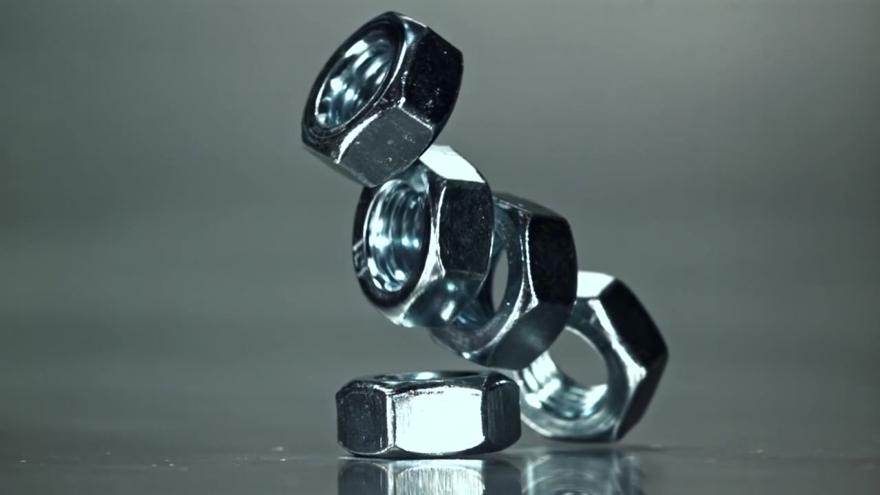 Metallmuttrar som faller och kollapsar i slow motion på grå bakgrund.