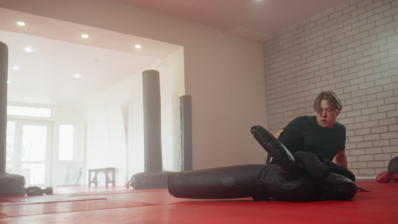 Policeman in black uniform performing ground combat training on dummy inside gym, practicing grappling and striking techniques on red mat, demonstrating focus, preparation for real-life defense scenarios