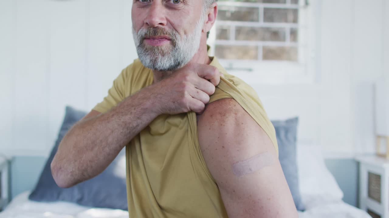 hombre maduro caucásico feliz que muestra un yeso en el brazo donde fue vacunado contra el coronavirus