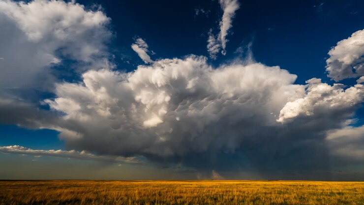 Clouds full of texture and contrast drift across a colorful sky and fields