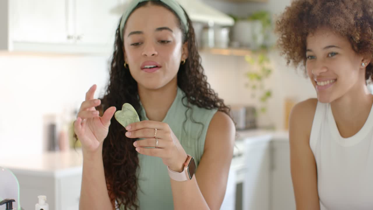 Donne afroamericane che iniziano una dimostrazione, disponendo dispositivi gua sha sul bancone della cucina e insegnando la cura della pelle.