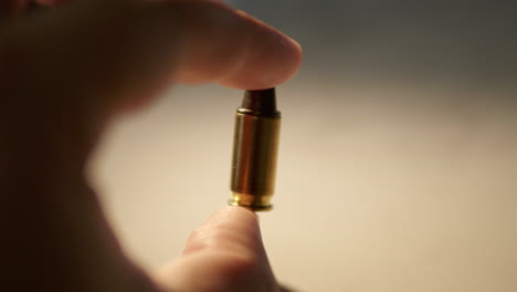 a close-up shot of an individual holding a single bullet between his thumb and forefinger