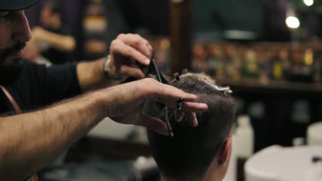 Vista-De-Cerca-De-Las-Manos-Del-Barbero-Realizando-Un-Corte-De-Pelo-Con-Tijeras-Sosteniendo-Un-Cepillo-En-Sus-Manos.-Tiro-En-Cámara-Lenta