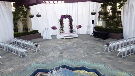 low altitude drone flying towards wedding stage, wedding ceremony under the open sky and fountain at the center of the hall