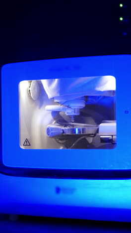 advanced technology in dentistry. works of the dental milling machine processing of carving out shape of human teeth in blue light. vertical video