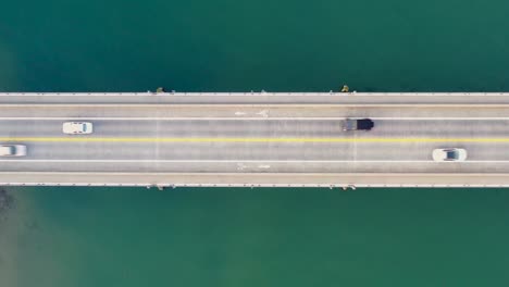 Toma-Aérea-Sobre-El-Agua-De-Autos-Cruzando-Un-Puente.