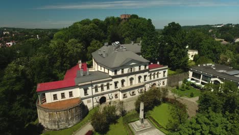 A-historic-and-restored-manor-house-on-a-hill,-surrounded-by-a-park-with-green-trees-during-summer-in-Poland,-captured-in-a-dynamic-4K-drone-shot