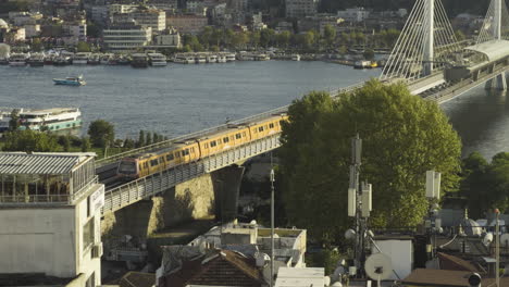 golden horn metro bridge crossing the water with the city skyline and distant historical landmarks visible as tram crosses at sunset