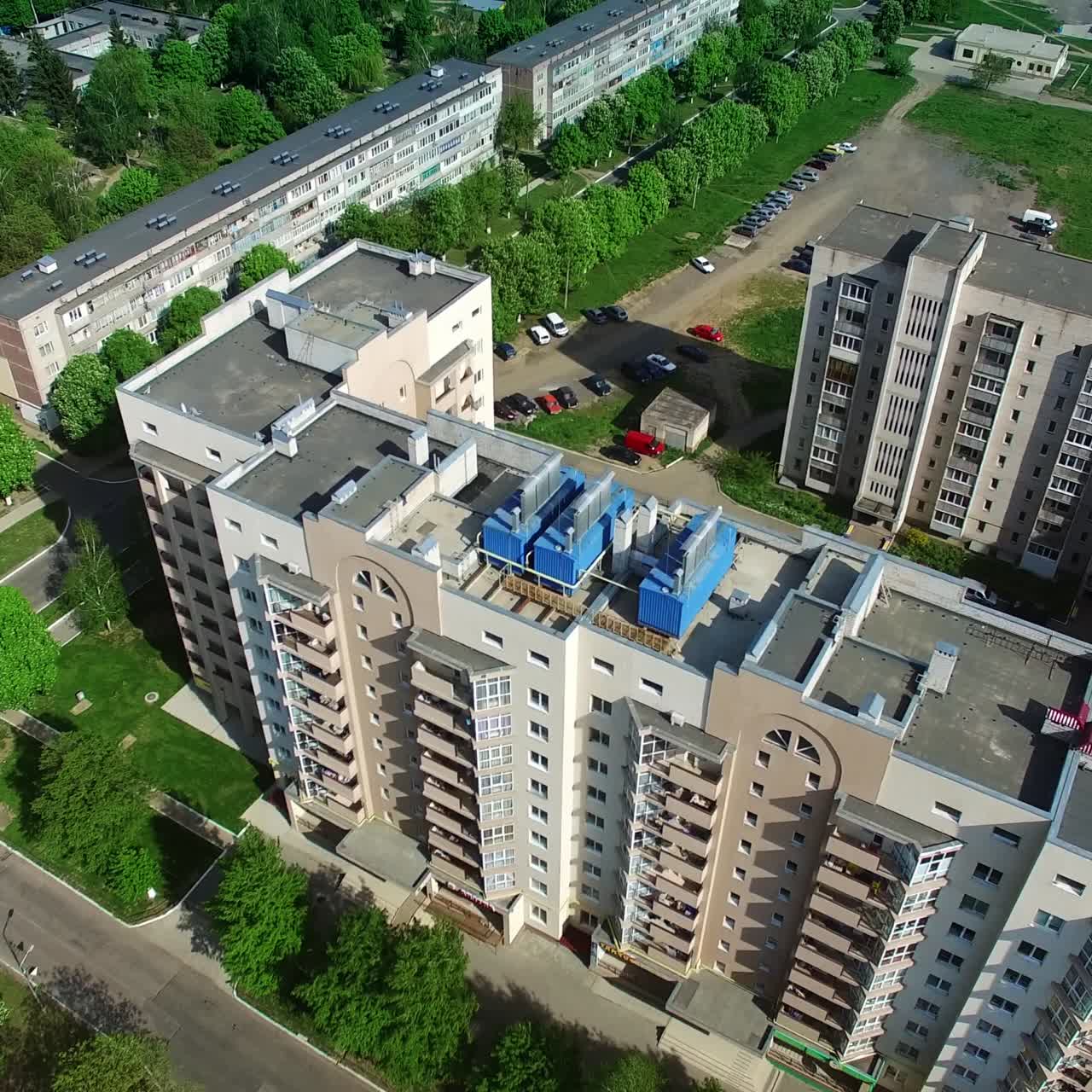Flying over the multi-storied buildings with nice well-kept territories around and lots of trees and greenery. View of the city from air