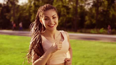 long hair woman with dreads running in park and turning her head around playing with her dreads looking in camera. slow motion