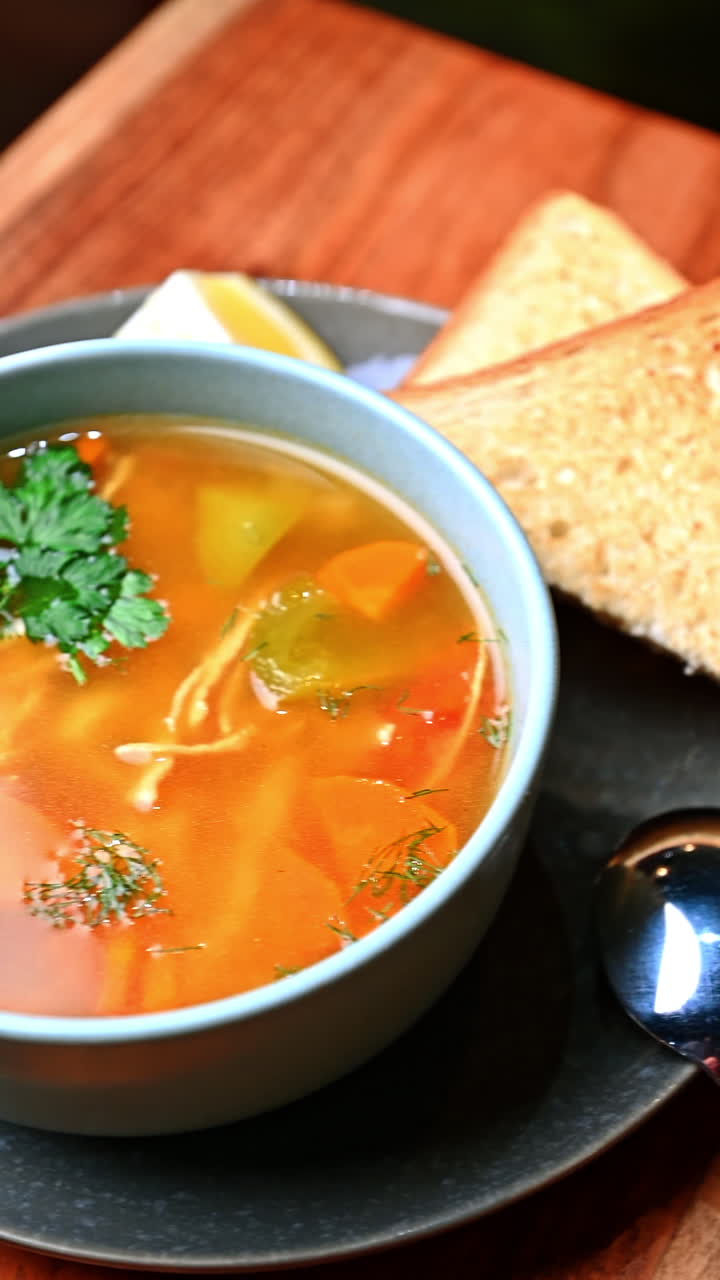 Homemade chicken soup with vegetables and toast bread. Bowl of clear chicken soup with vegetables and fresh herbs served with toasted bread on wooden table