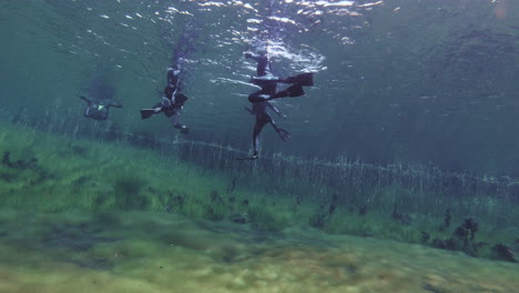 team of divers exploring natural limestone sinkhole pond in australia.