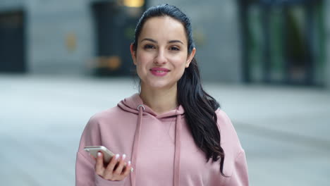 happy girl looking into camera, holding smartphone
