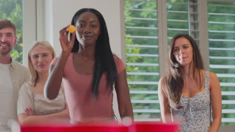 multi-cultural group of friends playing game at home together throwing ball into paper cup