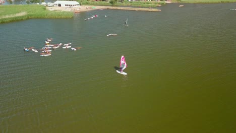 Encircling-aerial-shot,-camera-pans-up-from-the-group-of-idle-windsurfers,-revealing-the-cleary,-sunny-sky