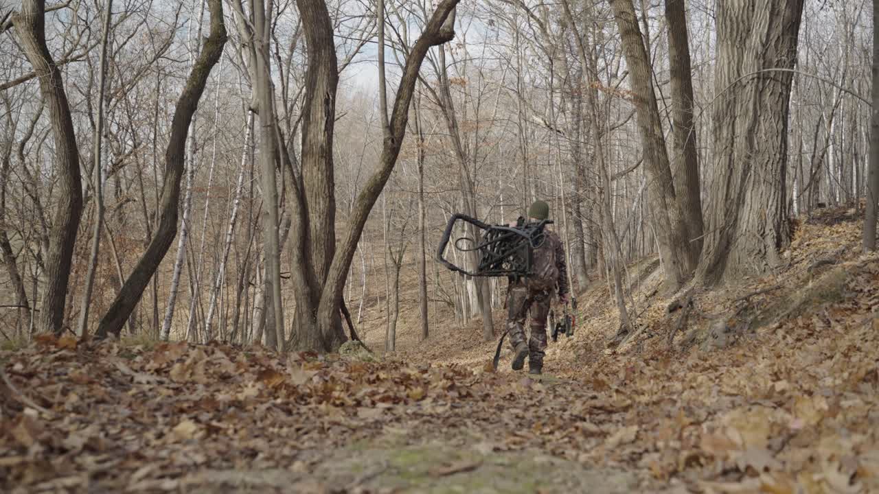 Gimbal following bowhunter in camouflage outfit walking in forest path during winter